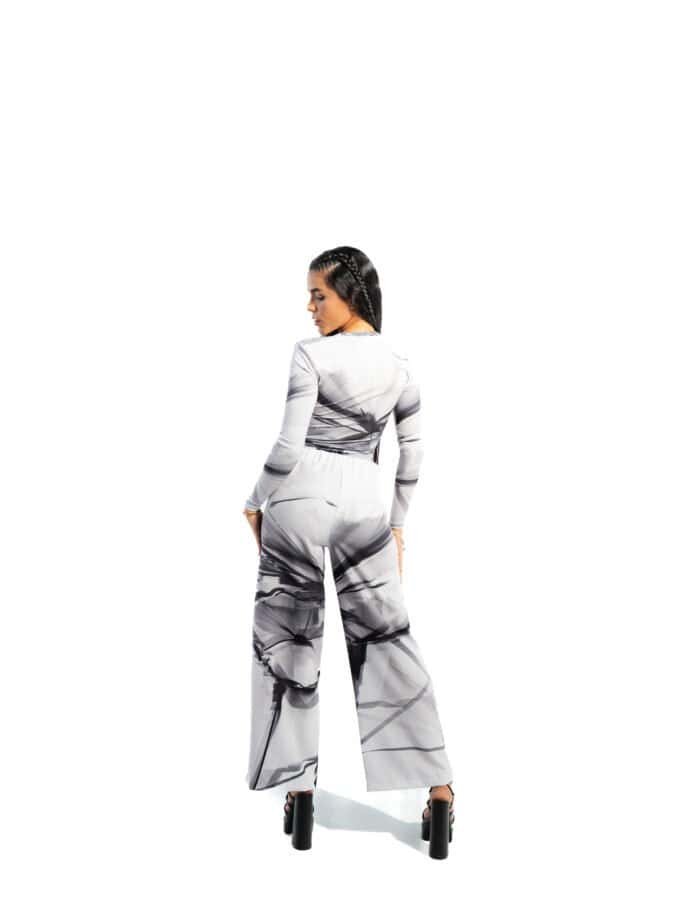 Elegant woman in black and white marble print jumpsuit, high-heeled shoes, standing against a white background, showcasing stylish fashion and modern design.