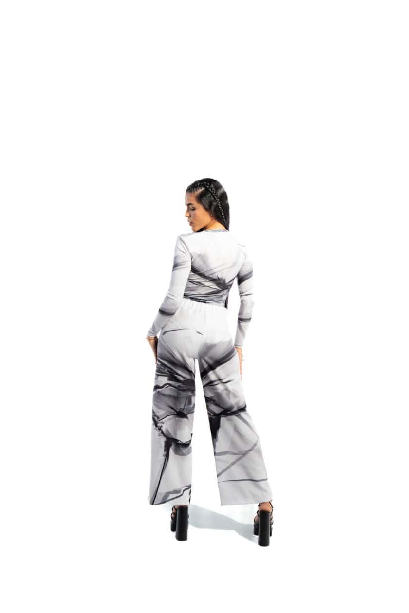 Elegant woman in black and white marble print jumpsuit, high-heeled shoes, standing against a white background, showcasing stylish fashion and modern design.