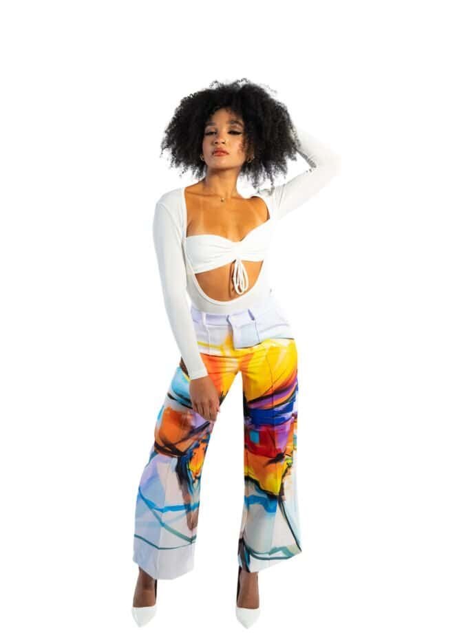 Colorful high-waisted pants with abstract art print, paired with a white cut-out crop top and white heels, creating a vibrant, fashionable look perfect for summer or casual outings.