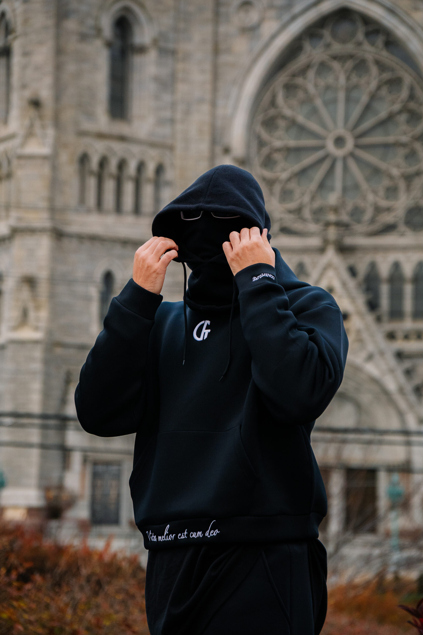 1. Close-up of a person in black hoodie with face hidden, standing in front of a historic cathedral, outdoor urban scene.