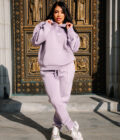 1. Woman in pastel lilac hoodie and joggers standing in front of ornate gold and black religious statue doorway in urban setting.