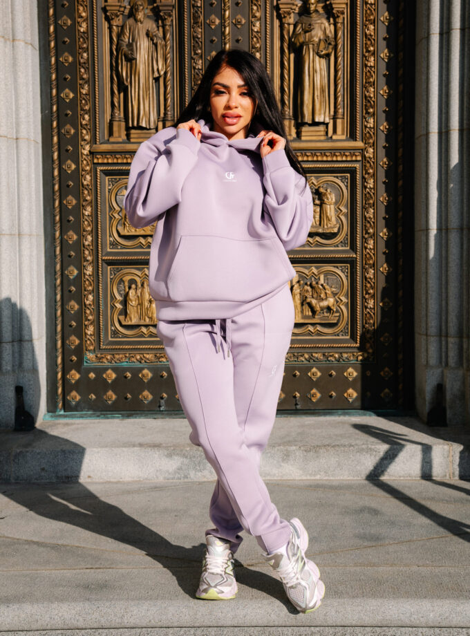 1. Woman in pastel lilac hoodie and joggers standing in front of ornate gold and black religious statue doorway in urban setting.