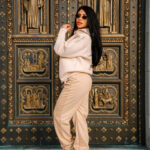 Elegant woman in beige hoodie and sweatpants posing in front of ornate church door, fashion style, urban streetwear, fall outfit, stylish casual attire, NYC fashion scene, trendy and comfortable.
