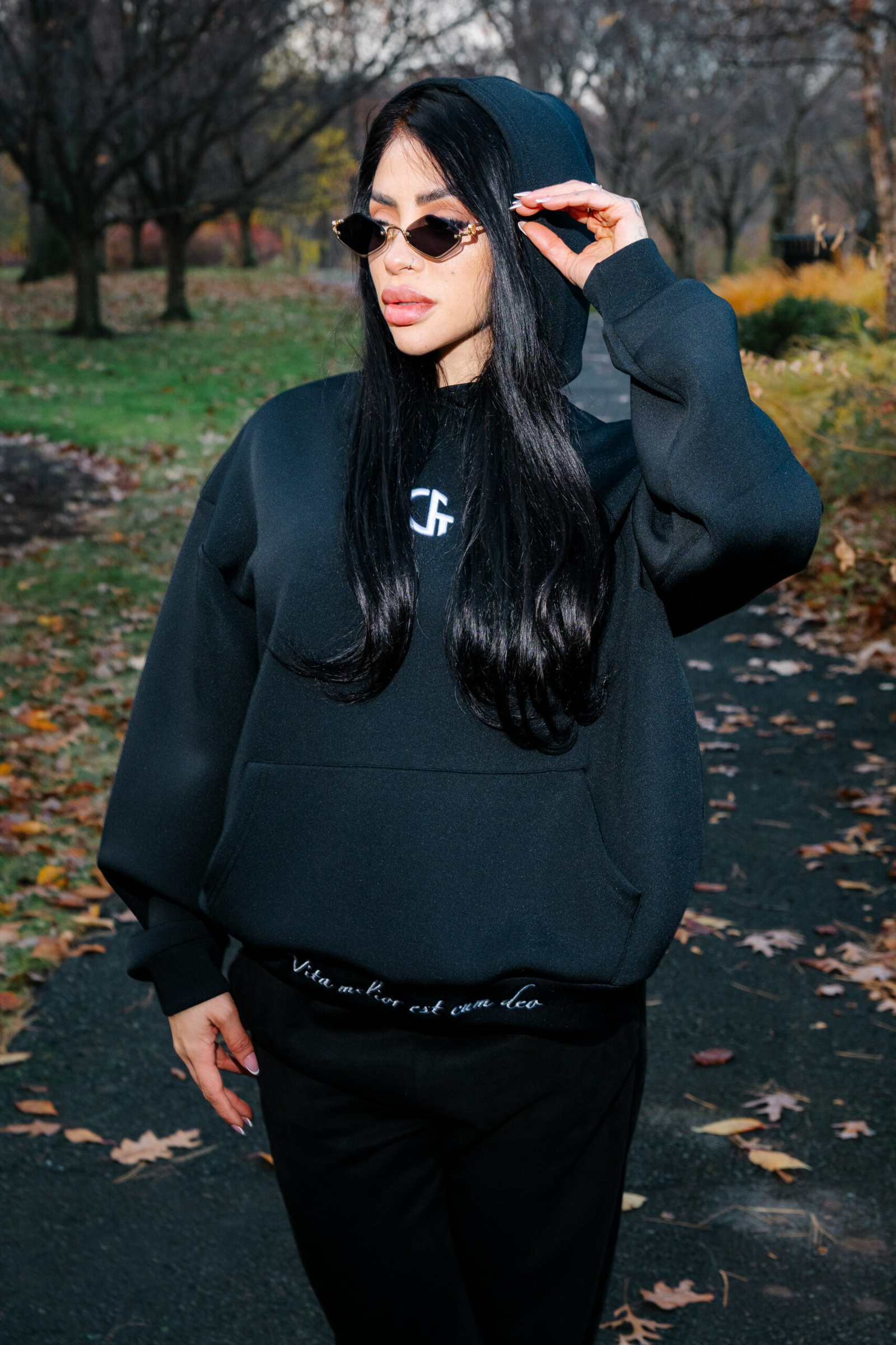 Stylish woman in black hoodie and sunglasses outdoors in autumn park, fashion, streetwear, fall scenery.