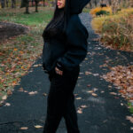 Cozy woman in black hoodie and sneakers standing on autumn park trail, showcasing casual fall fashion outdoors.