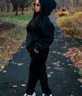 Cozy woman in black hoodie and sneakers standing on autumn park trail, showcasing casual fall fashion outdoors.