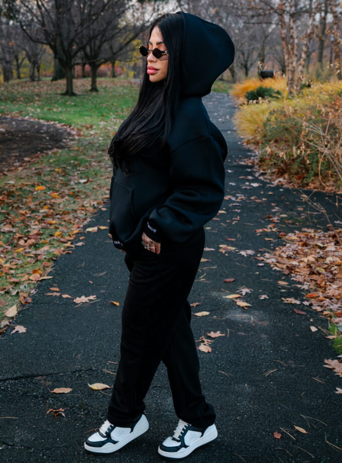 Cozy woman in black hoodie and sneakers standing on autumn park trail, showcasing casual fall fashion outdoors.